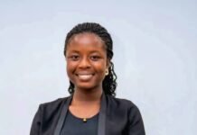 2025 OSVP Tech Queen Urges Young Women to Apply for Orange Social Venture Prize 2026 Young woman standing with folded hands, smiling, wearing a black blazer, black top, and bright orange skirt in a neutral setting.