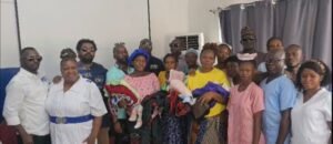 Diverse group of adults posing in a room, some in scrubs or traditional clothing, holding babies wrapped in blankets.