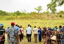 Joint UN-Government Field Visits Highlight Gains in Food Security, Healthcare and Women’s Empowerment A diverse group of people standing in a field, chatting near a low fence with a grassy open area and trees in the background.