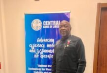 Rokel Bank CEO Dr. Walton Ekundayo Gilpin Elected WABA Vice President I at Monrovia Assembly Man in black traditional attire standing next to a blue Central Bank of Liberia banner in a doorway.