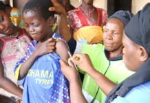 Sierra Leone Records 41 Measles Cases as Health Authorities Urge Immediate Vaccination Young person receiving a vaccine shot in the upper arm from a healthcare worker, with a group of community members watching nearby.