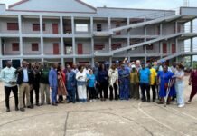 UN Agencies, Government Ministries Monitor Ready Salone Project at Central University Group of diverse people standing together for a photo in front of a gray building with red doors and external staircases, outdoors on a paved area, suggesting a community event or gathering.
