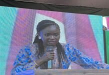 Sierra Leone Hosts WAIGF 2026 to Advance Internet Governance, Digital Inclusion and Regional Innovation A woman in a blue patterned dress speaks into a microphone at a podium on a stage with a colorful backdrop behind her.