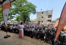 Orange SL Engages Prince of Wales Pupils on Cyberbullying, Excessive Screen Time Outdoor school assembly with hundreds of students listening to a speaker, banners on both sides, and a partially built brick building in the background.