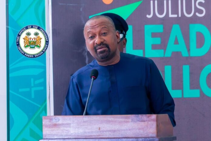 Vice President, Dr. Mohamed Juldeh Jalloh Man in a blue traditional outfit speaks at a wooden podium with a microphone, an official seal to his left and a backdrop with 'LEAD' text behind him, during an event.