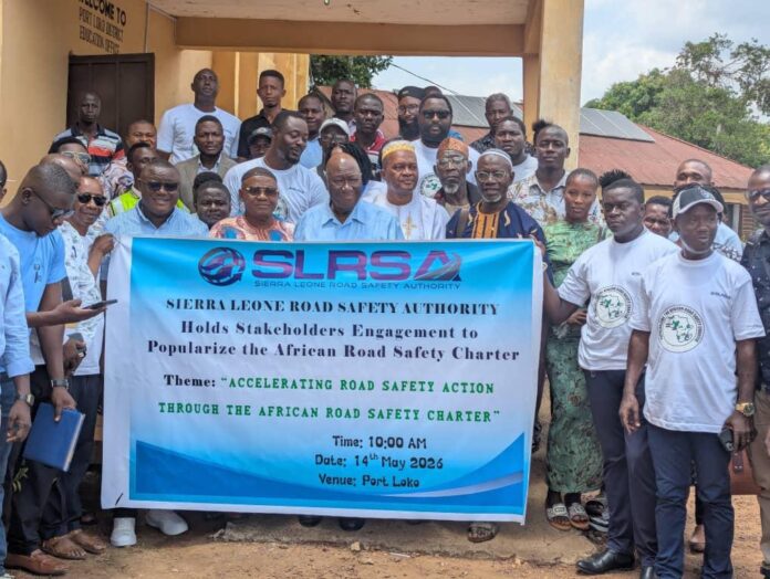 Group photo of diverse attendees posing outdoors behind a banner for the Sierra Leone Road Safety Authority stakeholder engagement on accelerating road safety action in Port Loko.