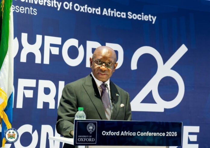 Man in a dark suit and glasses speaks at a lectern, with a blue backdrop reading 'Oxford Africa Conference 2026'.