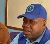 Govt. Assures Public of Ebola Preparedness, Confirms Sierra Leone Remains Ebola-Free Man wearing a blue cap and matching vest with an organization logo, seated at a table indoors.