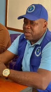 Man wearing a blue cap and matching vest with an organization logo, seated at a table indoors.