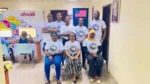 Group of eight people in matching white t-shirts posing for a team photo in a bright training room with Africell branding in the background.