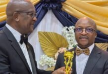Chief Justice Receives Prestigious Judicial Reform Award, Speaks on Leadership at 2026 West Africa Heroes Awards Two men in tuxedos share a moment at an award ceremony as one hands a gold trophy to the other, with decorative drapes in the background.