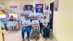 Eight people in matching white shirts pose for a team photo in a bright, tech-themed classroom with colorful mural and Africell branding in the background.