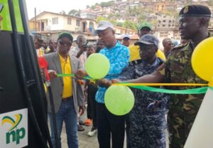 Officials cut a green ribbon at a ribbon-cutting ceremony, with balloons and a crowd near a bus displaying an np logo nearby onlookers celebrate the launch.