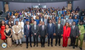 Large diverse group of professionals in formal attire posing for a group photo in a conference hall.