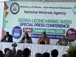 Panelists seated at a long table during a press conference, with a large banner behind reading Sierra Leone Mining Week and related agencies.