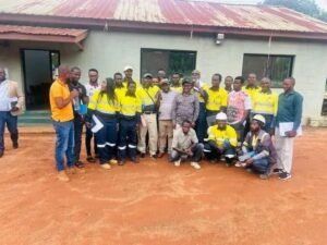 Group of people wearing yellow safety vests posing for a photo outside a building with a red metal roof, a training or team event in progress.