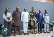 SLEF President Pushes for Modern Labour Laws, Urges Protection for Workers in Digital Economy Six people stand in a row posing for a group photo at an event; their attire ranges from traditional to formal, with a circular logo featuring a fist and globe in the lower left.