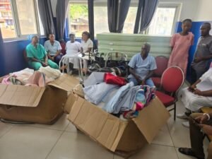 People sit in a bright room beside open boxes overflowing with blankets and clothes for donation distribution.