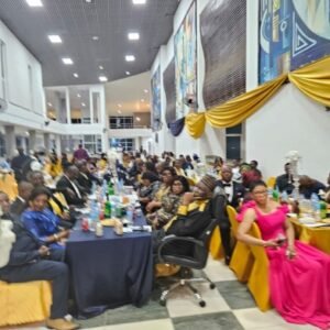 A crowded banquet hall with long tables, guests in formal attire, blue tablecloths and gold decorations along the walls.