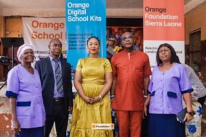 Group of five people pose for a photo at an Orange Foundation Sierra Leone event, with banners for Orange School Kits behind them.