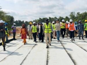 Group of people in safety vests and hard hats walking on a concrete construction site, with palm trees in the background.