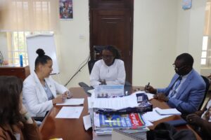Four professionals sit around a wooden conference table in an office, discussing with papers and magazines spread out in front of them.