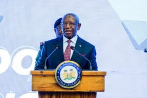 Speakers at a podium with Sierra Leone seal, delivering a formal address in a suit and tie.