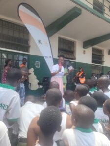 Group of students gathered outside a school around a tall curved banner with white, orange, and green sections during an event.
