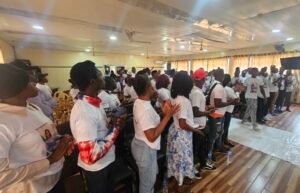 Large group of people in white shirts standing and clapping in a hall during an event.
