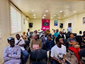 Diverse audience seated in a conference room, attentively watching a presentation at the front of the room.