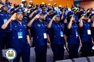 Group of uniformed officials in blue attire saluting during an official ceremony, with the presidential seal visible in the foreground.