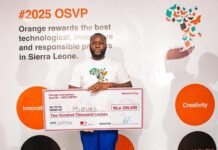 OSVP 2025 Winner Edward Kamara Inspires Young Innovators to Seize Opportunities and Apply for 2026 Prize Man holding an oversized cheque for Two Hundred Thousand Leones at a #2025 OSVP event; backdrop shows orange circles with Innovation, Creativity, Technology, and Industrialization labels.
