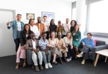 Wiener Zeitung Showcases Innovation-Driven Journalism Model to African Media Fellows in Austria Group of diverse colleagues posing together in a bright office, smiling and waving at the camera.