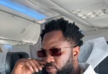 Dauda Jalloh, Husband of Admire Bio, Declared Wanted by Sierra Leone Police Portrait of a man with a beard and sunglasses seated inside an airplane cabin, wearing a white shirt and a gold chain.