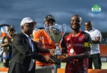 Orange FA Cup: East End Lions Crowned 2026 Champions Man in a suit hands a silver trophy to a soccer player in an orange jersey during an awards ceremony under a blue sky.