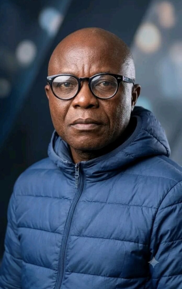 Portrait of a middle-aged man wearing round black glasses and a blue puffer jacket, looking at the camera.
