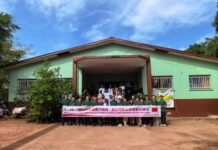 27th Chinese Medical Team Launches Public Welfare Outreach on International Day of Action for Women’s Health Group of people standing in front of a green building on a sunny day, holding a banner for a community event.