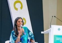 Human Capital Development Critical to Aviation Safety and Sustainability, SLCAA DG Avers Woman in a blue patterned dress sits on a stage, speaking into a handheld microphone at a conference.