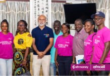 Africell & Afrimoney Strengthen Digital Inclusion Through University Connect and ACE Exercise Group of eight people posing for a photo at a community event; several wear pink 'Africell-Ace Exercise' shirts, with Afrimoney and Africell logos visible on a banner/bracelet.