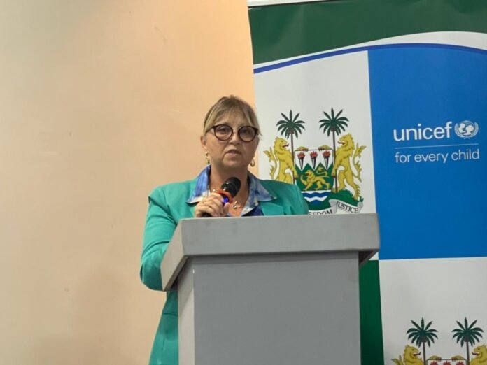 Woman in a teal blazer speaks at a podium with a UNICEF backdrop behind her.