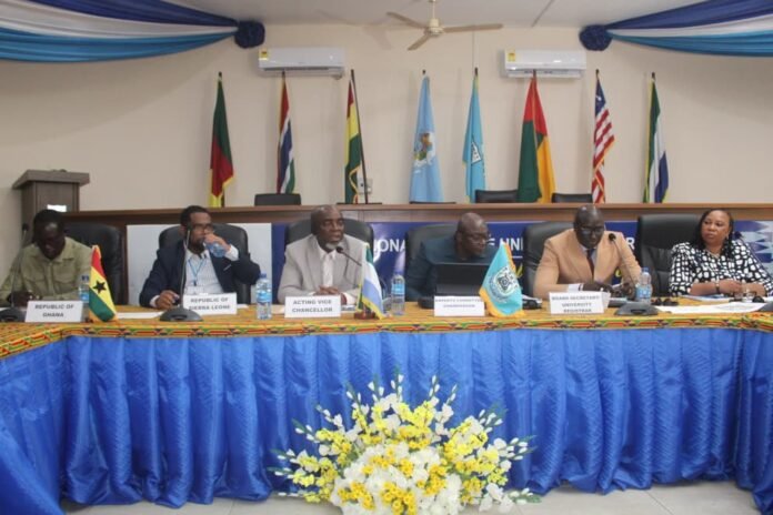 Six officials seated at a long panel table in a conference room, with microphones and nameplates, flags behind them and a blue tablecloth with a yellow floral arrangement in front.