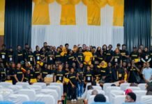98 Graduate from Spark Media Masterclass, Receive Professional Certification Large group of people in black shirts posing on a stage with a gold and white backdrop at a conference.