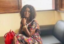 Sierra Leonean Woman Killed in Tragic Carjacking Incident in the United States Woman with curly hair in a colorful floral outfit sits on a black couch, resting her chin on her hand, with a red handbag beside her and sunlight coming through a window.