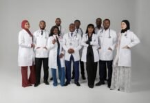 Sierra Leone Celebrates 25 Graduates From Russian Universities, 10 Qualify as Medical Doctors Diverse group of doctors and medical professionals posing together in white lab coats and stethoscopes in a studio setting.
