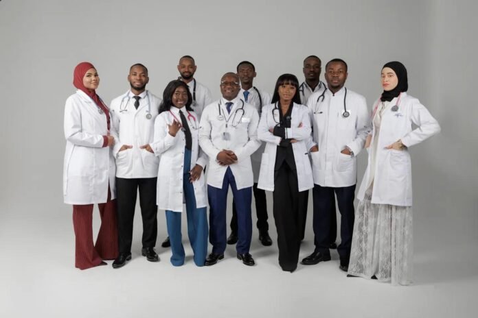 Diverse group of doctors and medical professionals posing together in white lab coats and stethoscopes in a studio setting.