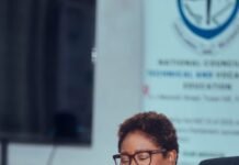 Edleen B. Elba Chairs Inaugural NCTVE Council Meeting, Charts New Course for TVET Reform Smiling woman with short curly hair and glasses, seated at a table with papers and a blue pen in a meeting room.