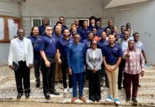 Government, A2MEND Explore New Opportunities for Higher Education and Youth Development Large group of professionals posing on tiled steps outside a building, many in navy polo shirts and others in business attire, facing the camera and smiling.