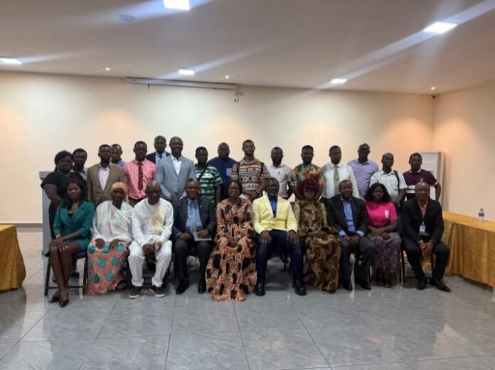 Group of professionals posing for a group photo in a conference room, with two rows of people seated and standing in formal and traditional attire.
