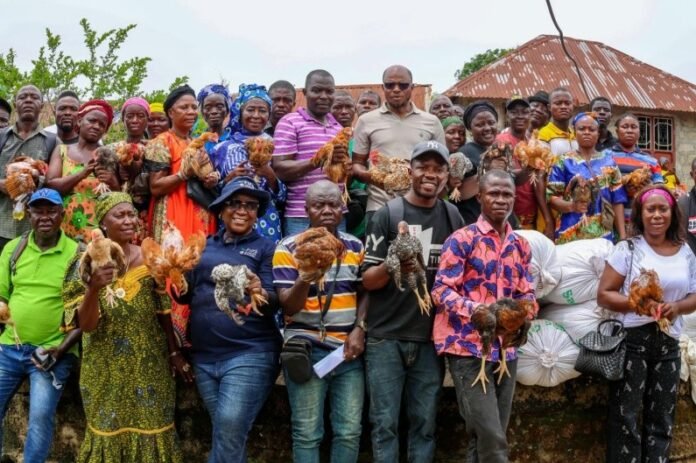 Group of people outdoors holding chickens, posing for a community event photo with a rural backdrop behind them.