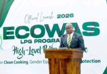 ECOWAS Marks 51: Amb. John Azunah Highlights Achievements and Sierra Leone’s Early Warning Progress Man in a suit delivering a speech at a wooden podium during the ECOWAS LPG Program 2026 official launch, with a banner in green and white behind him. It highlights Clean Cooking and gender equality themes.